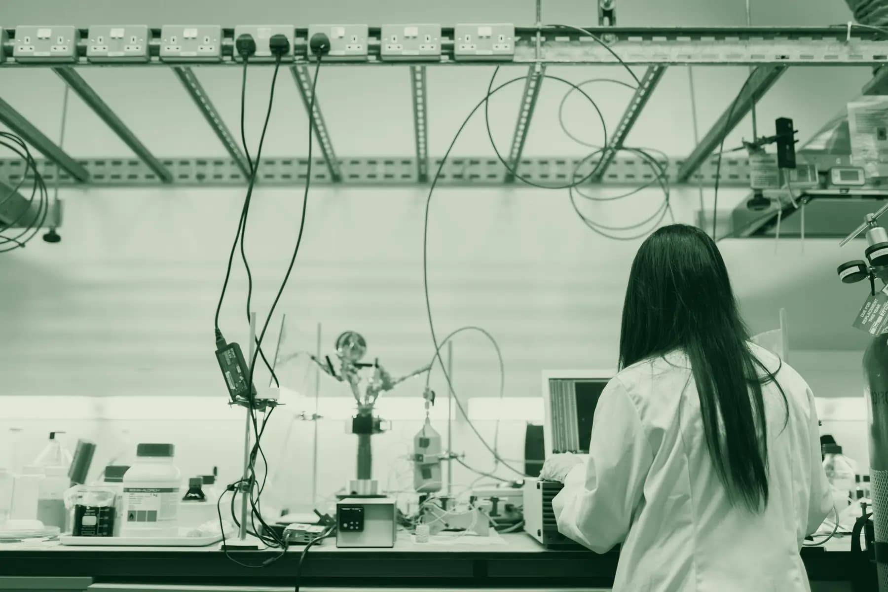 Pesquisadora em laboratório de eletrônica, cercada de cabos e instrumentos